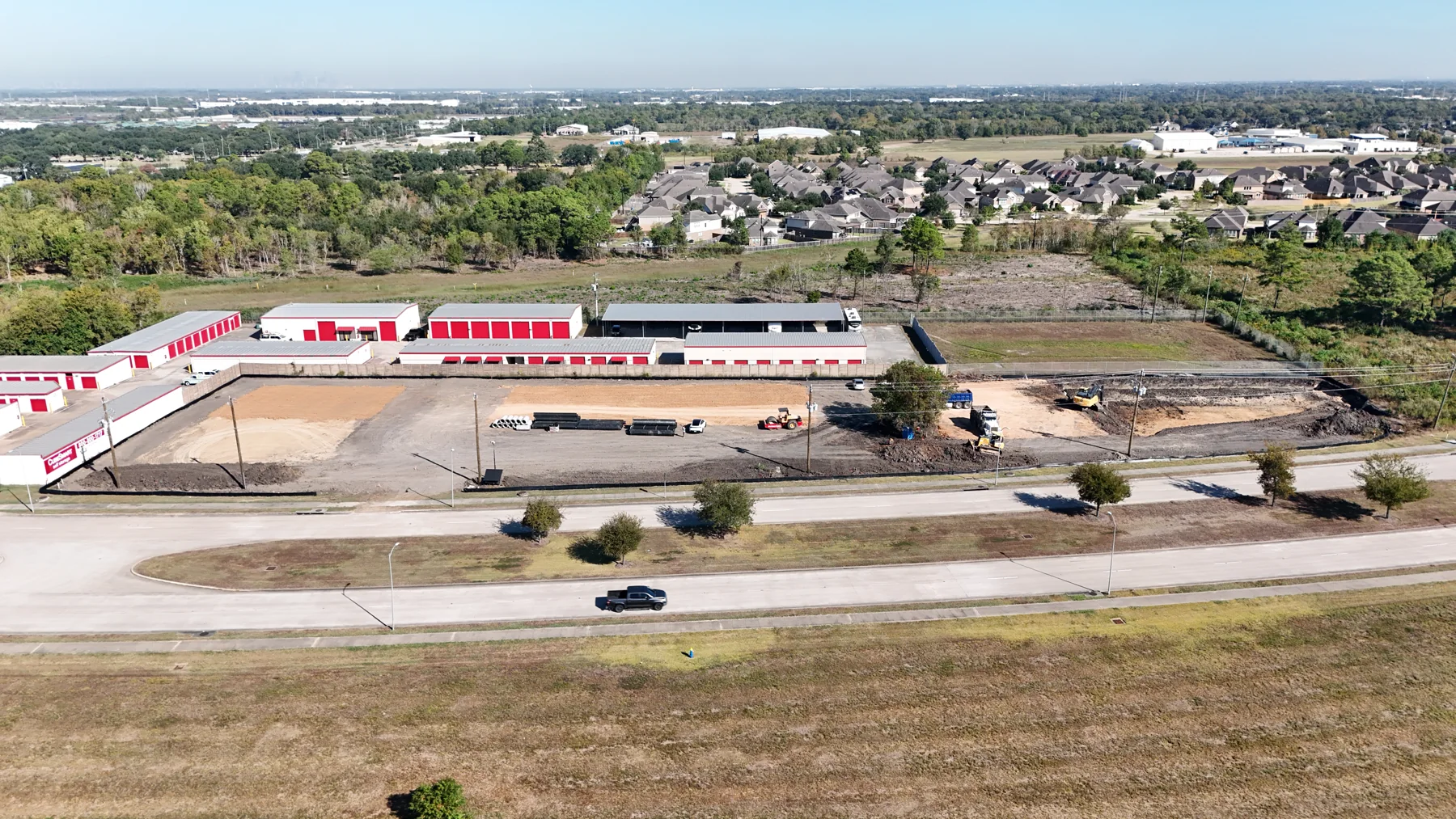 McHard Flex construction site on October 23, 2026: graded ground, staged drainage pipes and earthwork; red-door storage buildings behind the site belong to the neighboring property